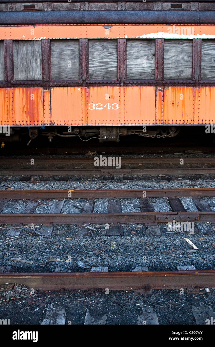 The rusting side of an old abandoned train carriage, with the numbers 3243. The car's windows are boarded up with wood. Stock Photo