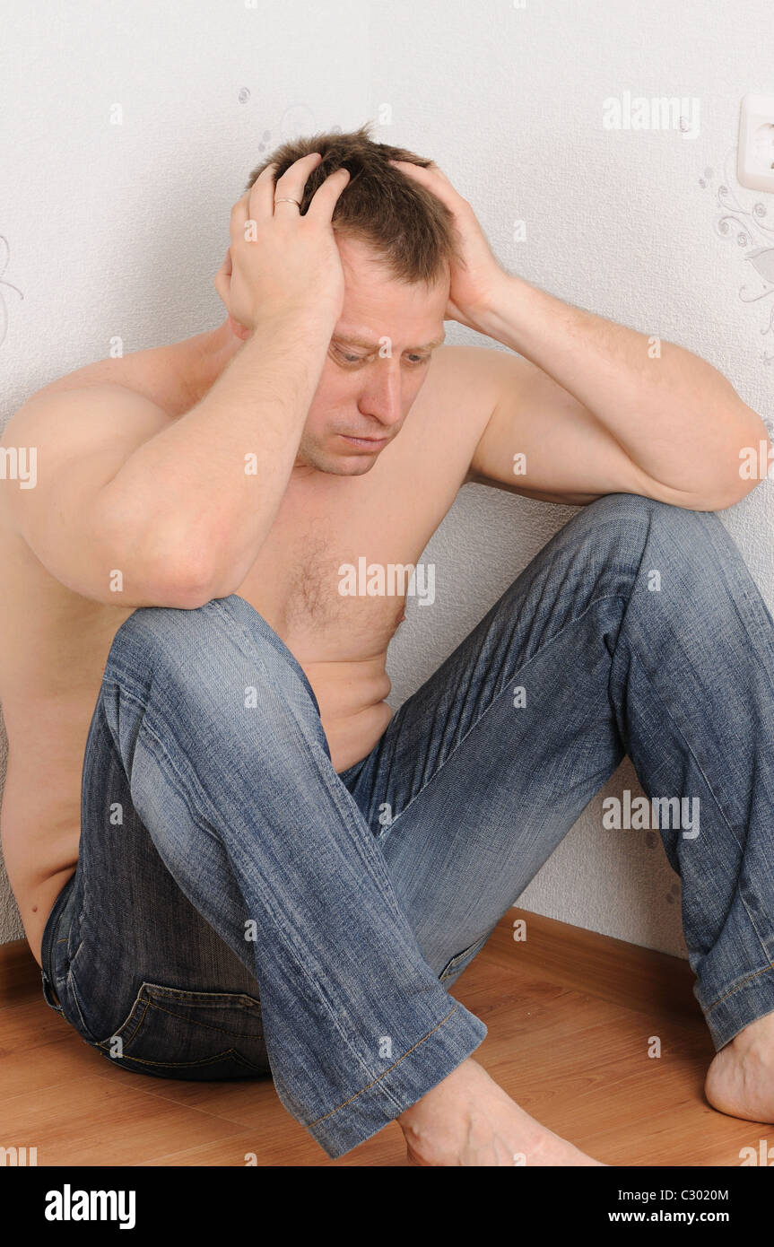 Upset the man sits in a corner of a room Stock Photo - Alamy