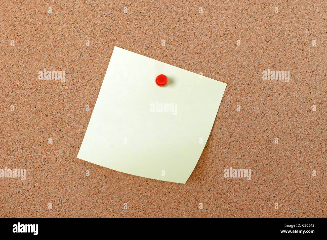 Yellow note paper attached with red pin to corkboard. Empty space for design. Stock Photo