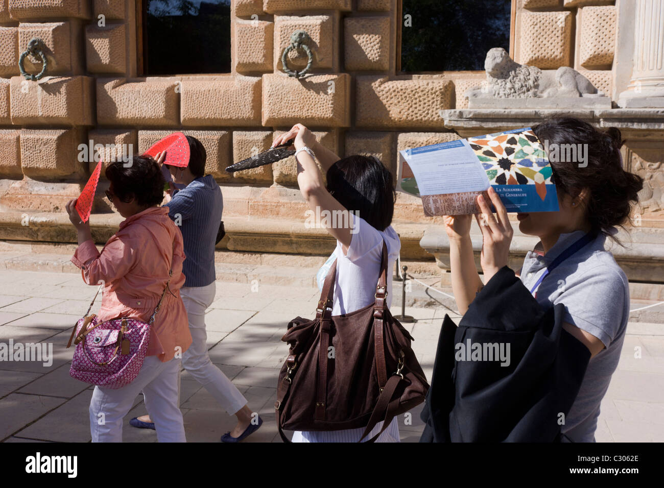 Two women tourists from Asia walk in the sunshine at Alhambra, both holding cameras. Stock Photo