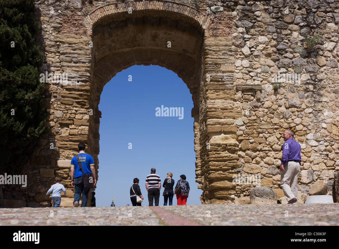 Visitors to the Andulucian town of Antequera, walk beneath the gated entrance of the Moorish Alcazaba Castle. Stock Photo