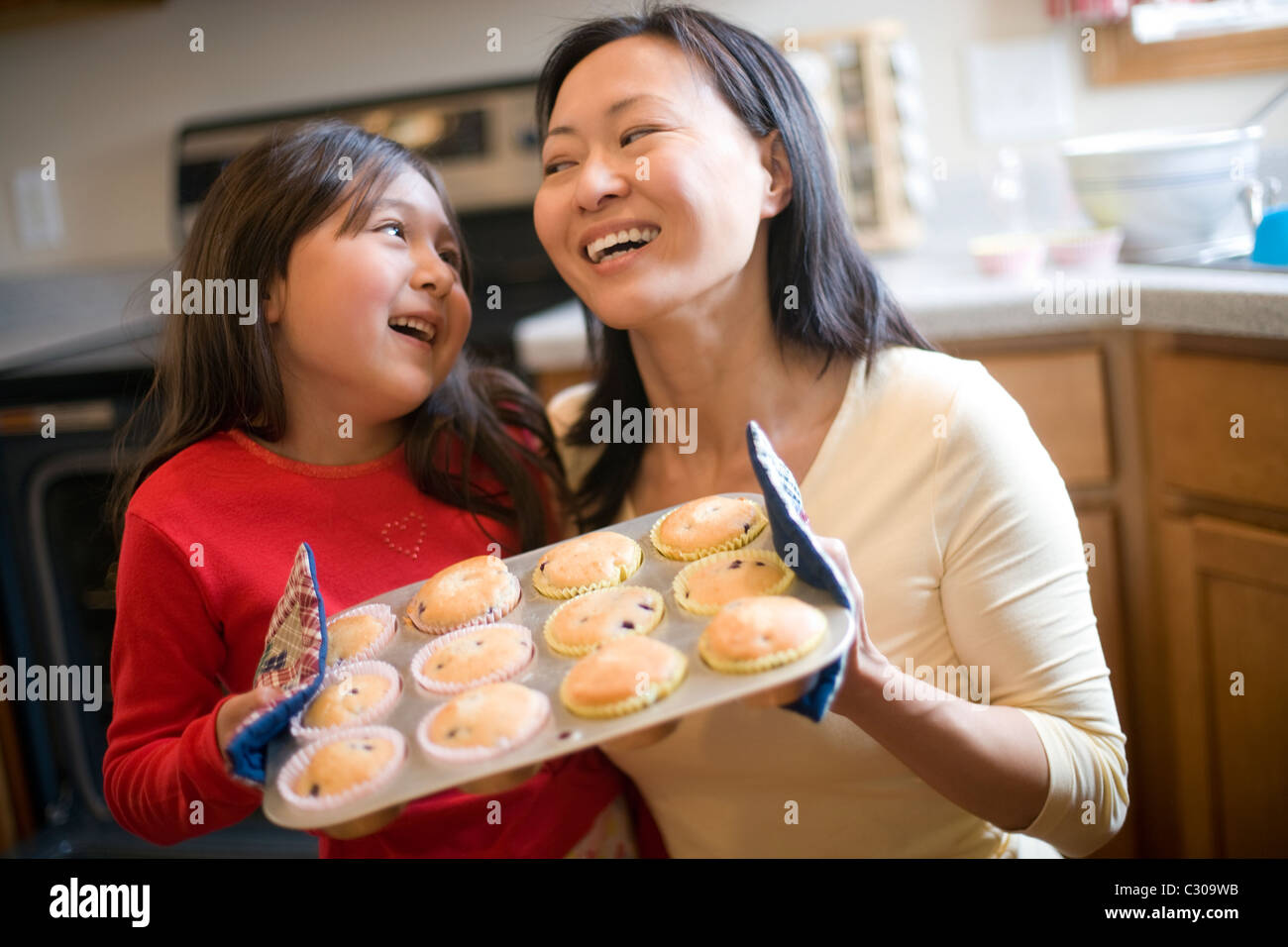 Asian mother and daughter baking muffins in the kitchen at home Stock Photo