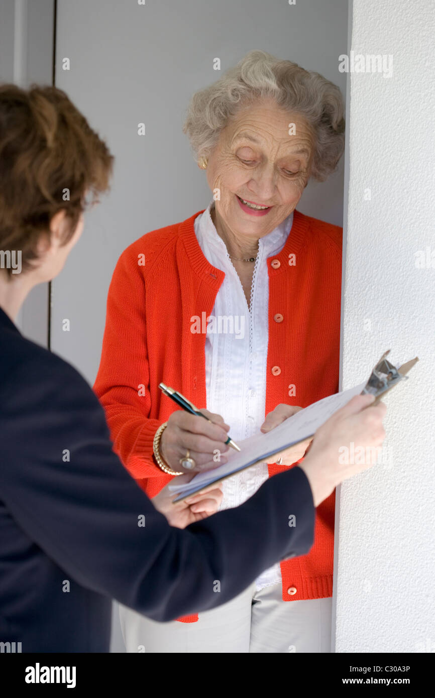 Attractive senior woman signing a document at her front door Stock Photo