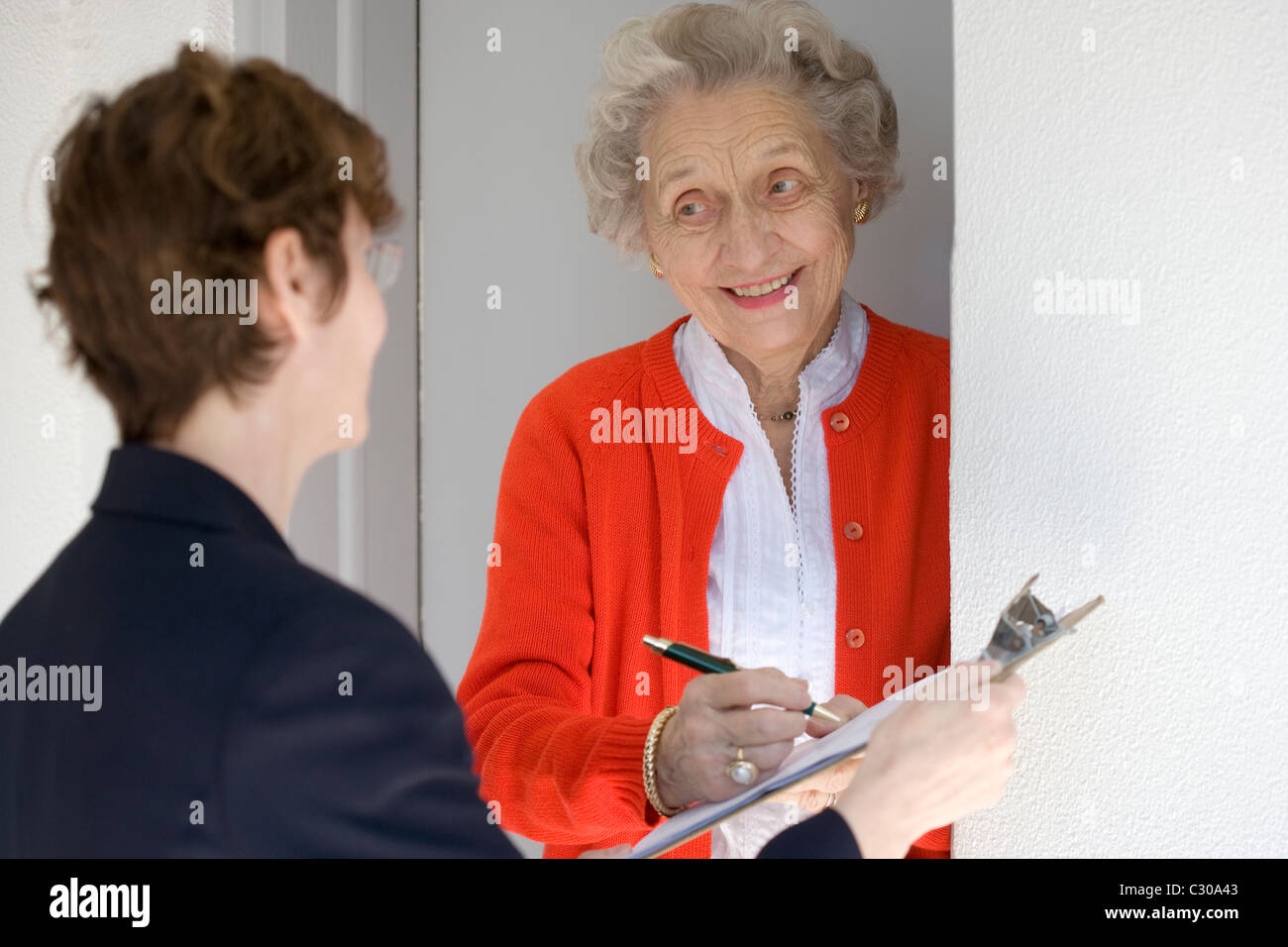 Attractive senior woman signing a document at her front door Stock Photo