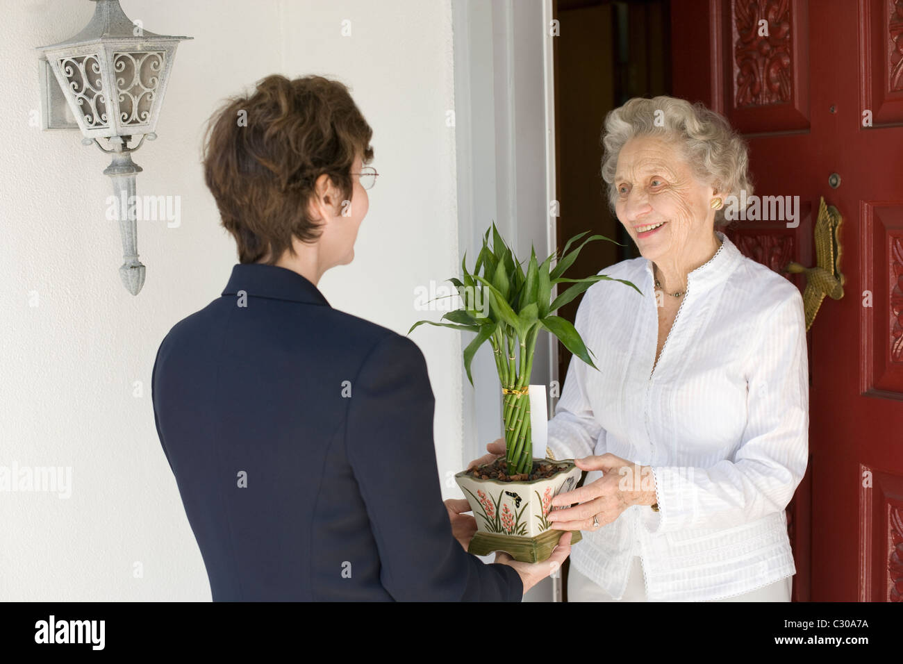 Attractive senior woman receiving gift of bamboo plant at front door Stock Photo