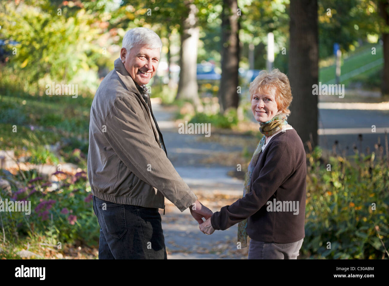 Senior couple walking along the sidewalk looking back at the camera Stock Photo