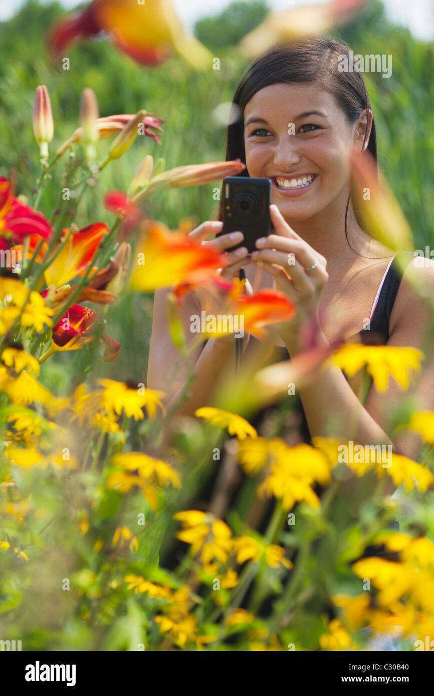 Cute Asian woman smiles while taking pictures of flowers with a small camera. Vertical shot. Stock Photo