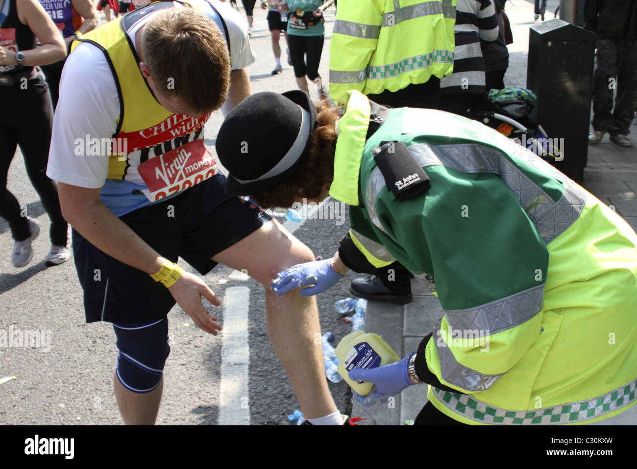 'St John Ambulance' volunteer provides medical assistance to runner on route of London Marathon Stock Photo