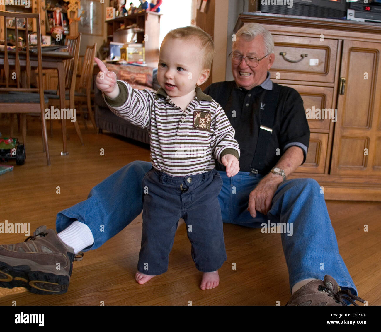 15 month old baby boy taking his first steps as his grandfather watches. Stock Photo