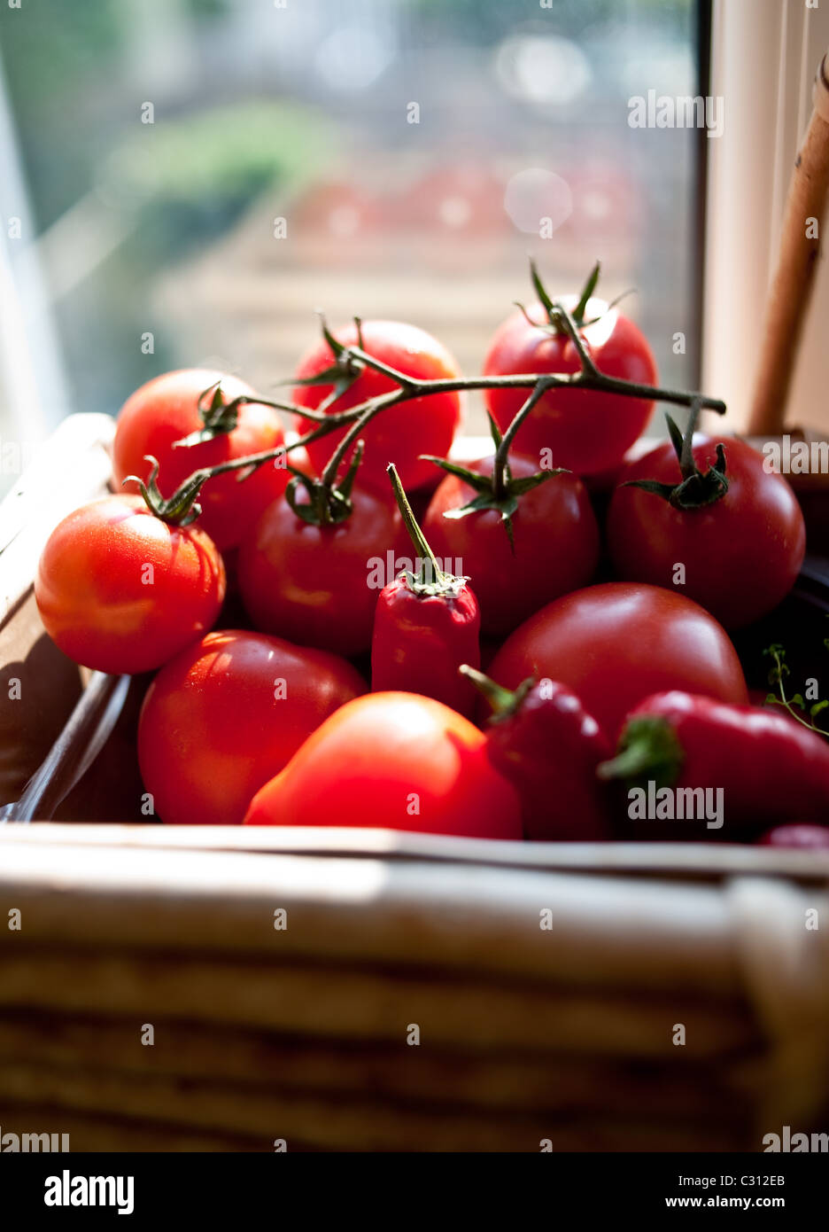 Vine tomatoes and chillies ripening in the sun on a kitchen window sill in a basket Stock Photo