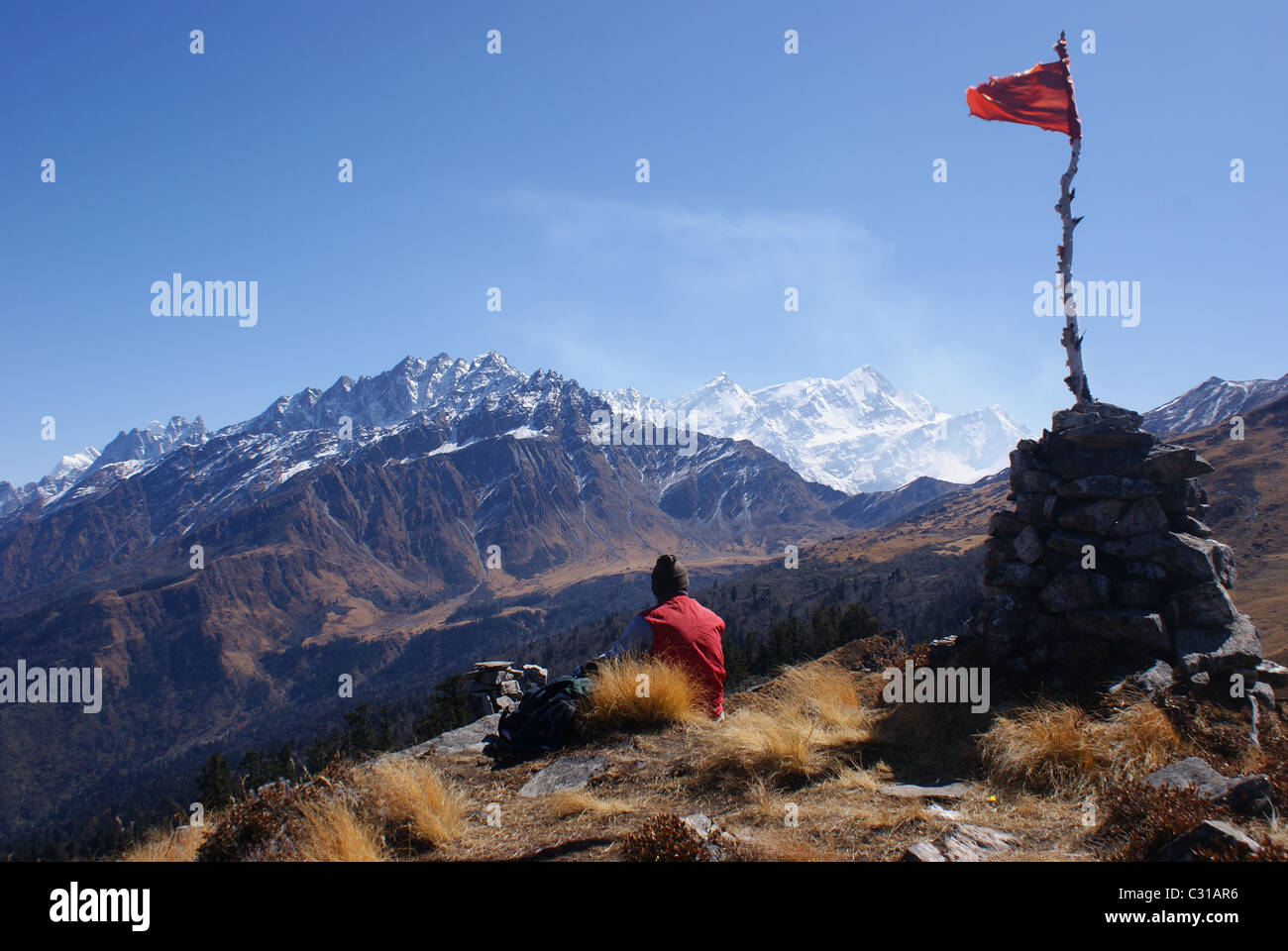Garhwal Himalayas, India: A trekker sits beneath a prayer flag near the legendary viewpoint of the Kuari Pass. Stock Photo