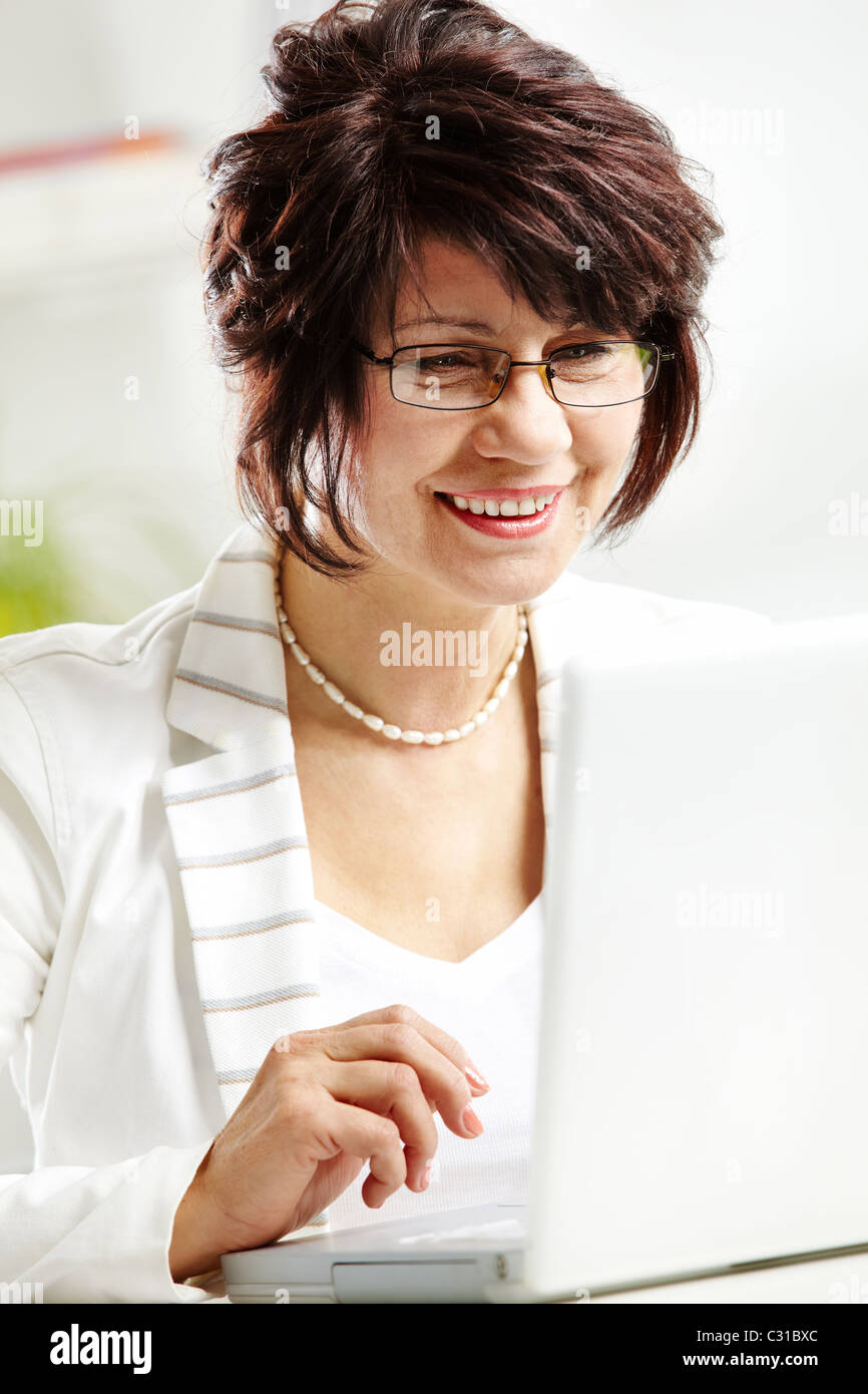 Portrait of middle-aged female typing and looking at laptop display Stock Photo