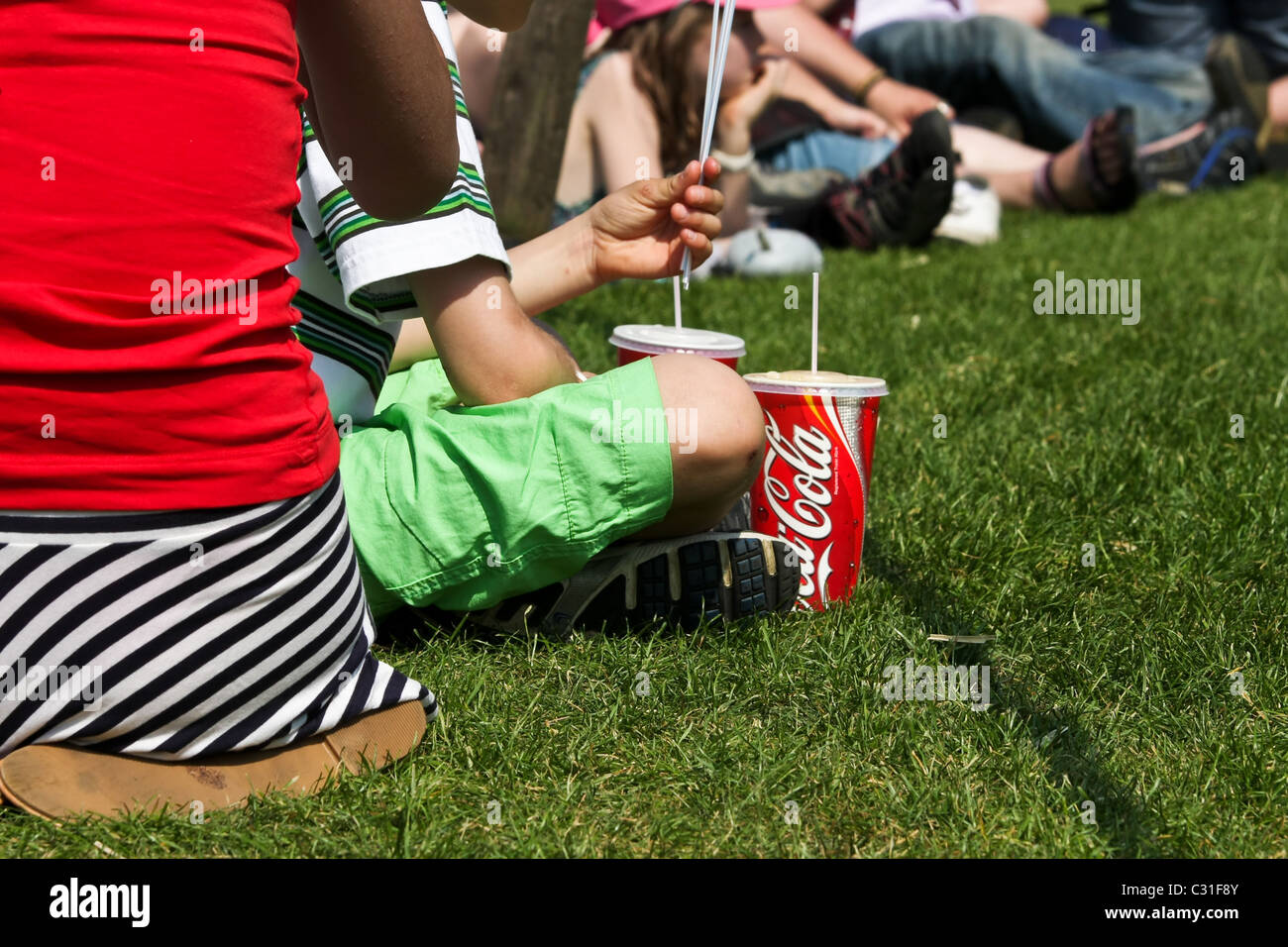 Children (unidentifiable) sitting on the grass and drinking coca cola Stock Photo