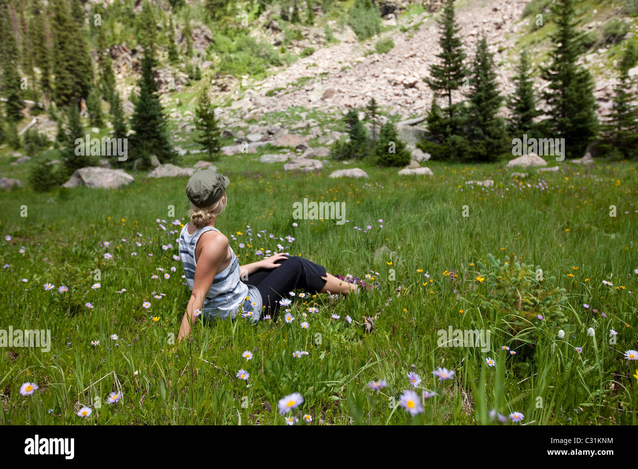 A young woman sits peacefully in a field of wildflowers enjoying the view. Stock Photo