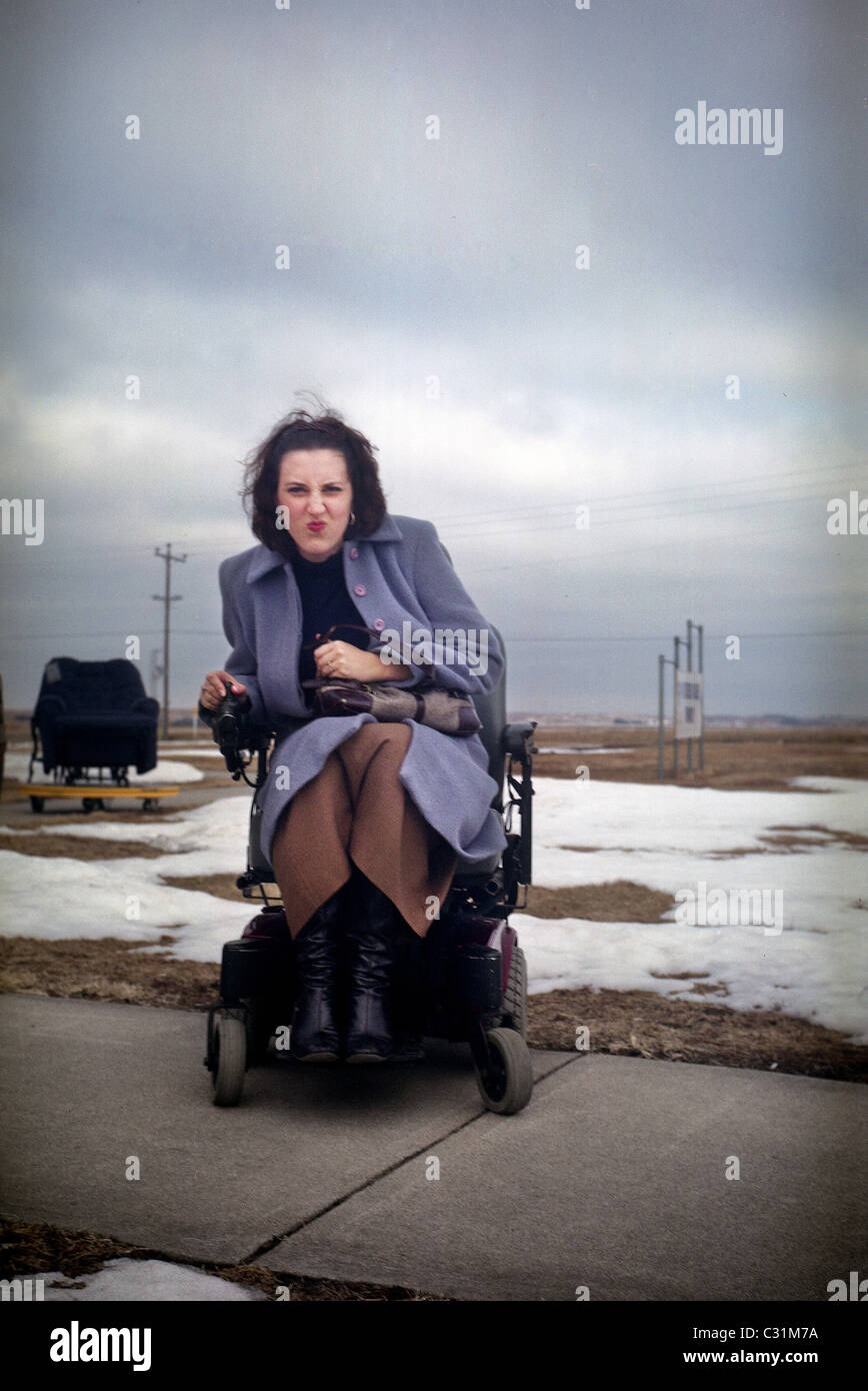 A young woman looks grumpy as she sits in a motorized wheelchair. Stock Photo