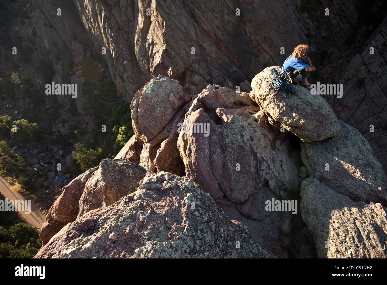 A young adult rock climber sits on the edge of a cliff after climbing a