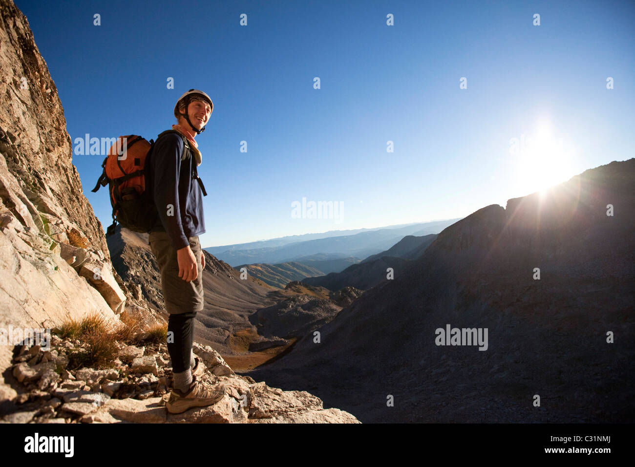 A young man smiles as the sunrises on his mountain climb. Stock Photo
