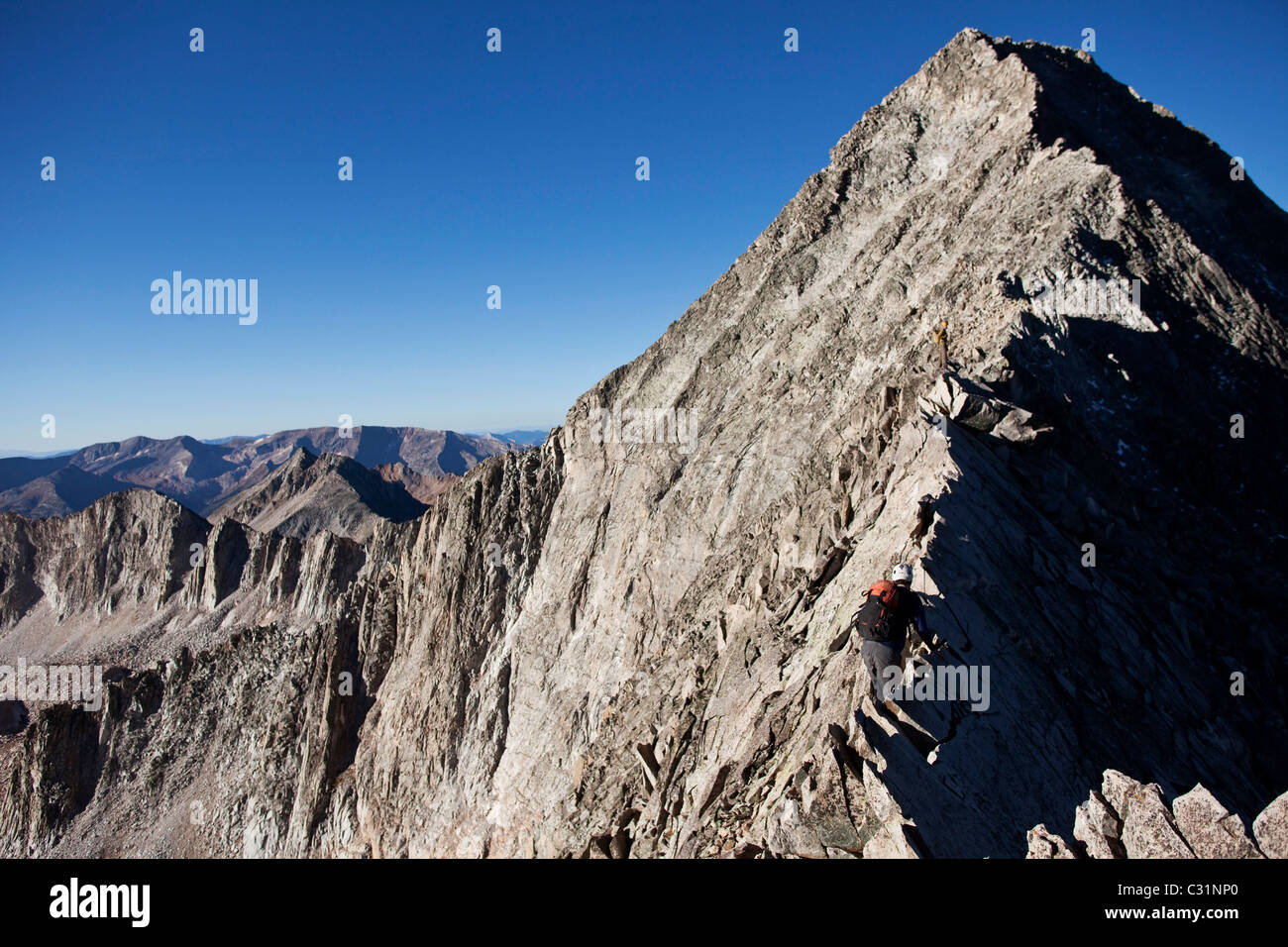 Two young men crossing an exposed ridge line with the summit behind them. Stock Photo