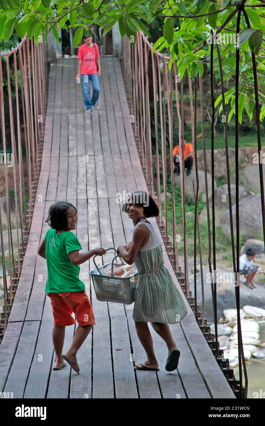 CHILDREN WITH A FOOD BASKET CROSSING THE STREAM ON A HANGING WOODEN BRIDGE, RANONG HOT SPRINGS, THAILAND, ASIA Stock Photo