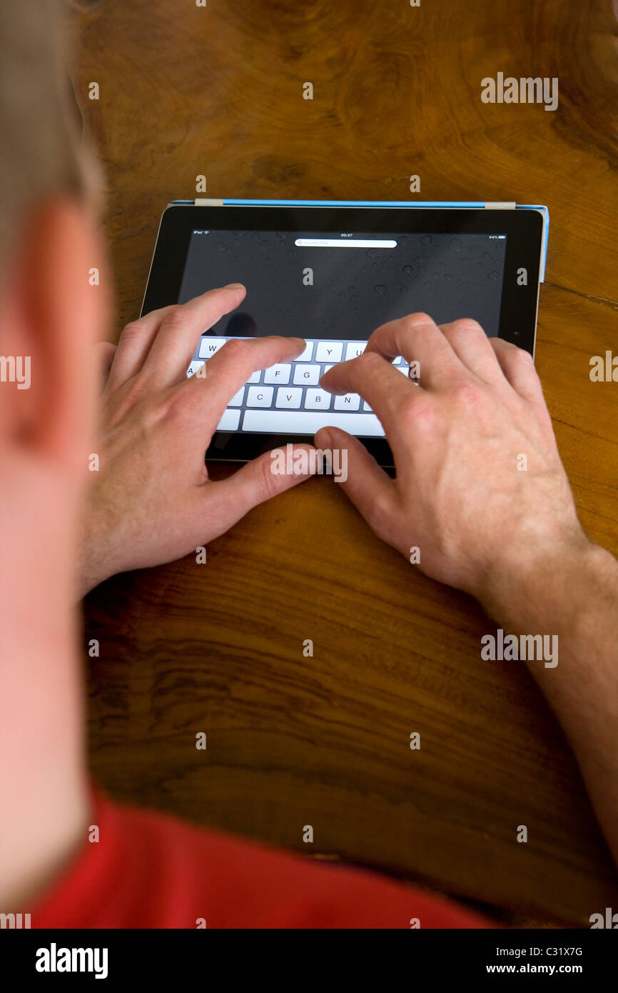 A man typing on his Ipad 2 using the apple smart cover for a stand. Stock Photo