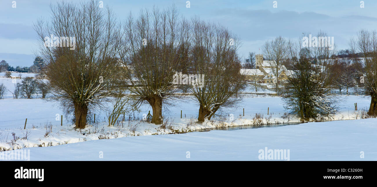 Church and snowy fields by the River Windrush in the village Swinbrook, The Cotswolds, UK Stock Photo