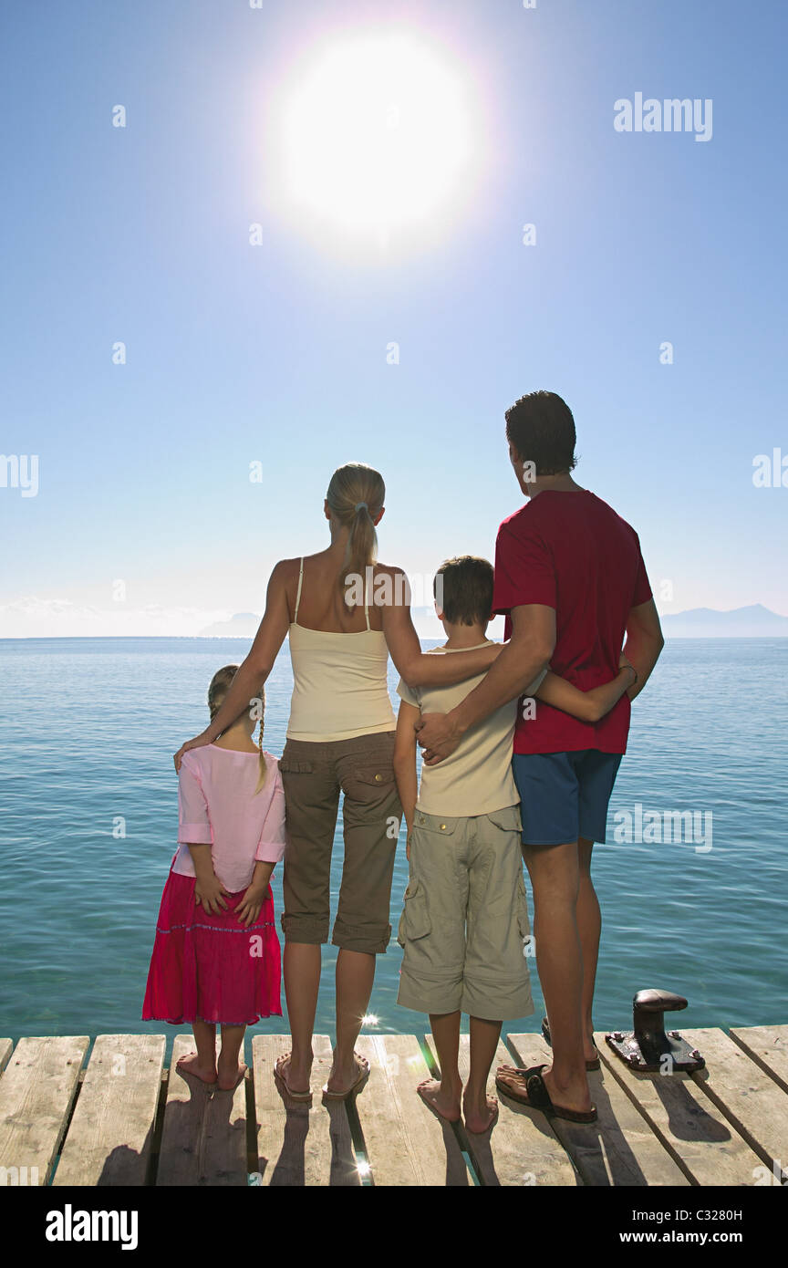 Rear view of family standing on jetty with sun shining Stock Photo