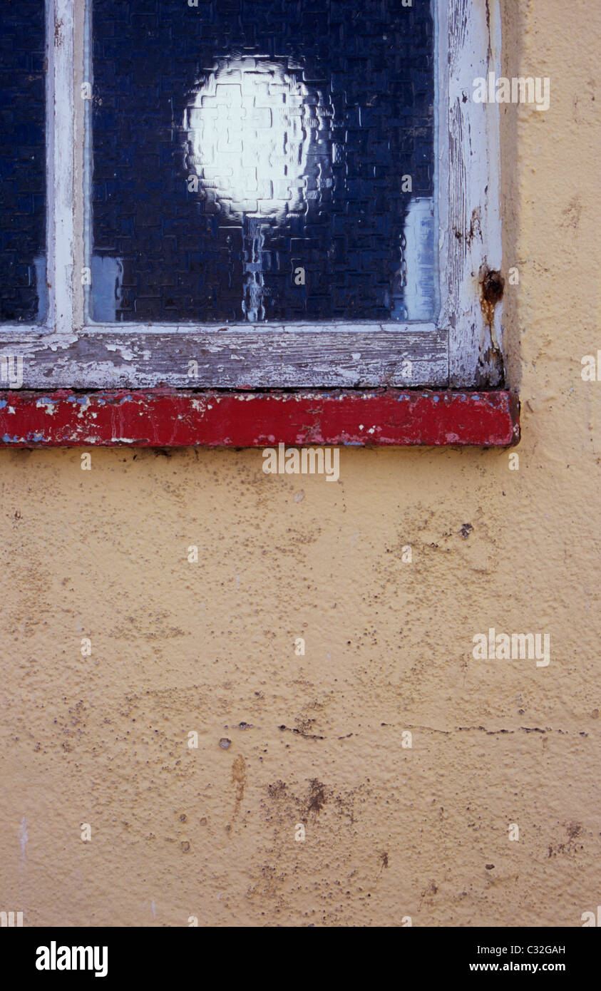 View from backyard of neglected wall and bathroom window with shaving mirror and bottle of mouthwash visible Stock Photo