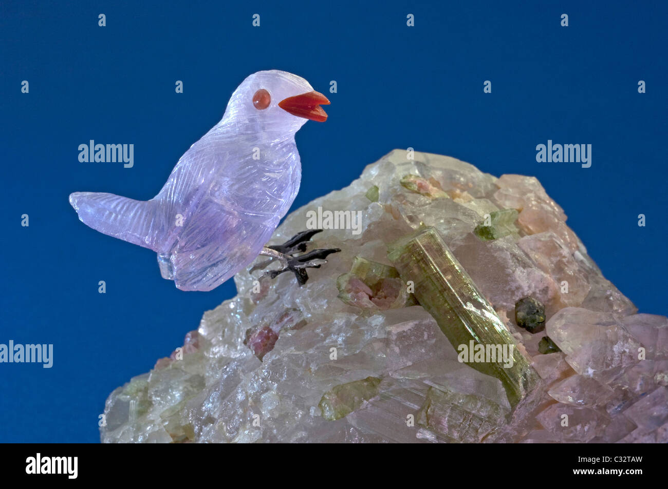 Sparrow made of Amethyst standing on a crystal with tourmaline. Studio picture against a blue background. Stock Photo