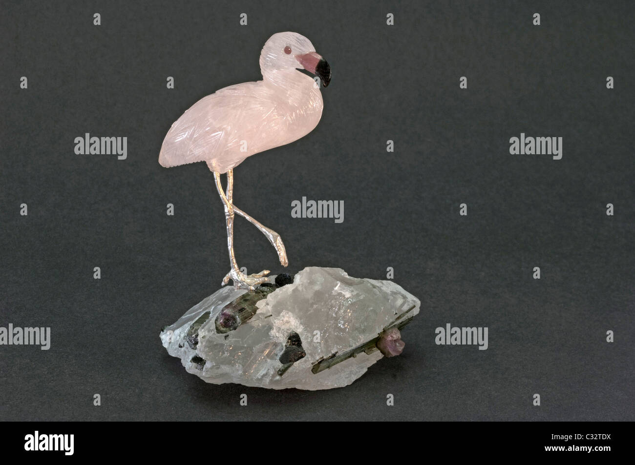 Flamingo made of Rose Quartz standing on a crystal with tourmaline. Studio picture against a blue background. Stock Photo