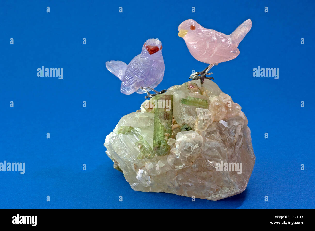 Sparrows made of Rose Quartz and Amethyst standing on a crystal with tourmaline. Studio picture against a blue background. Stock Photo