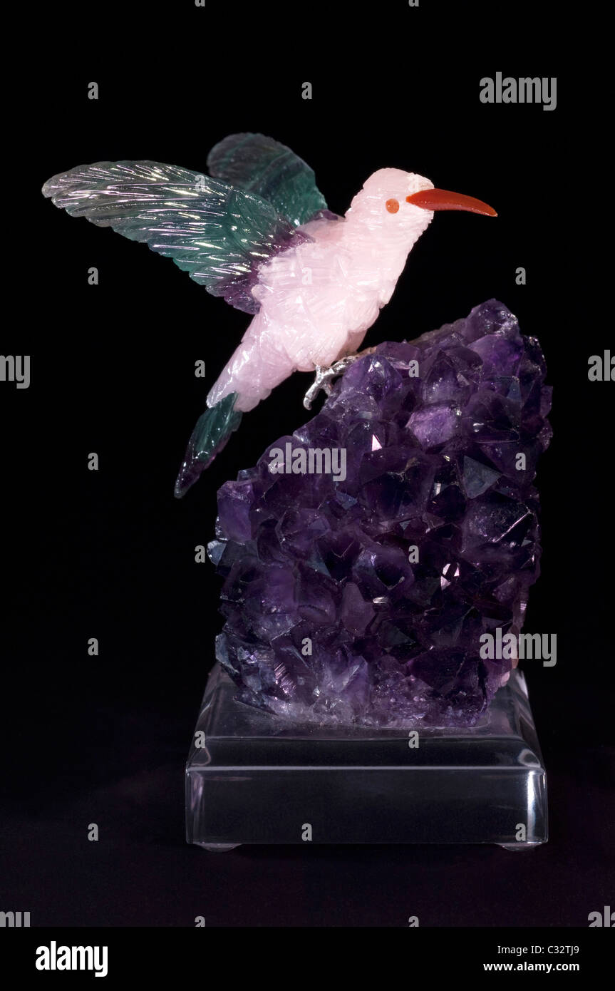 Colibri made of Rose Quartz and Fluorite landing on Amethyst. Studio picture against a dark background. Stock Photo