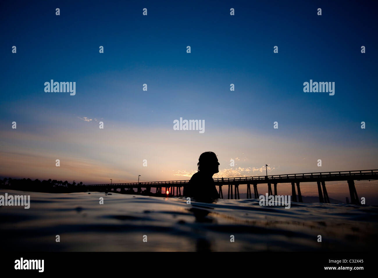 A male surfer watches the sunrise at Port Hueneme beach in Oxnard ...
