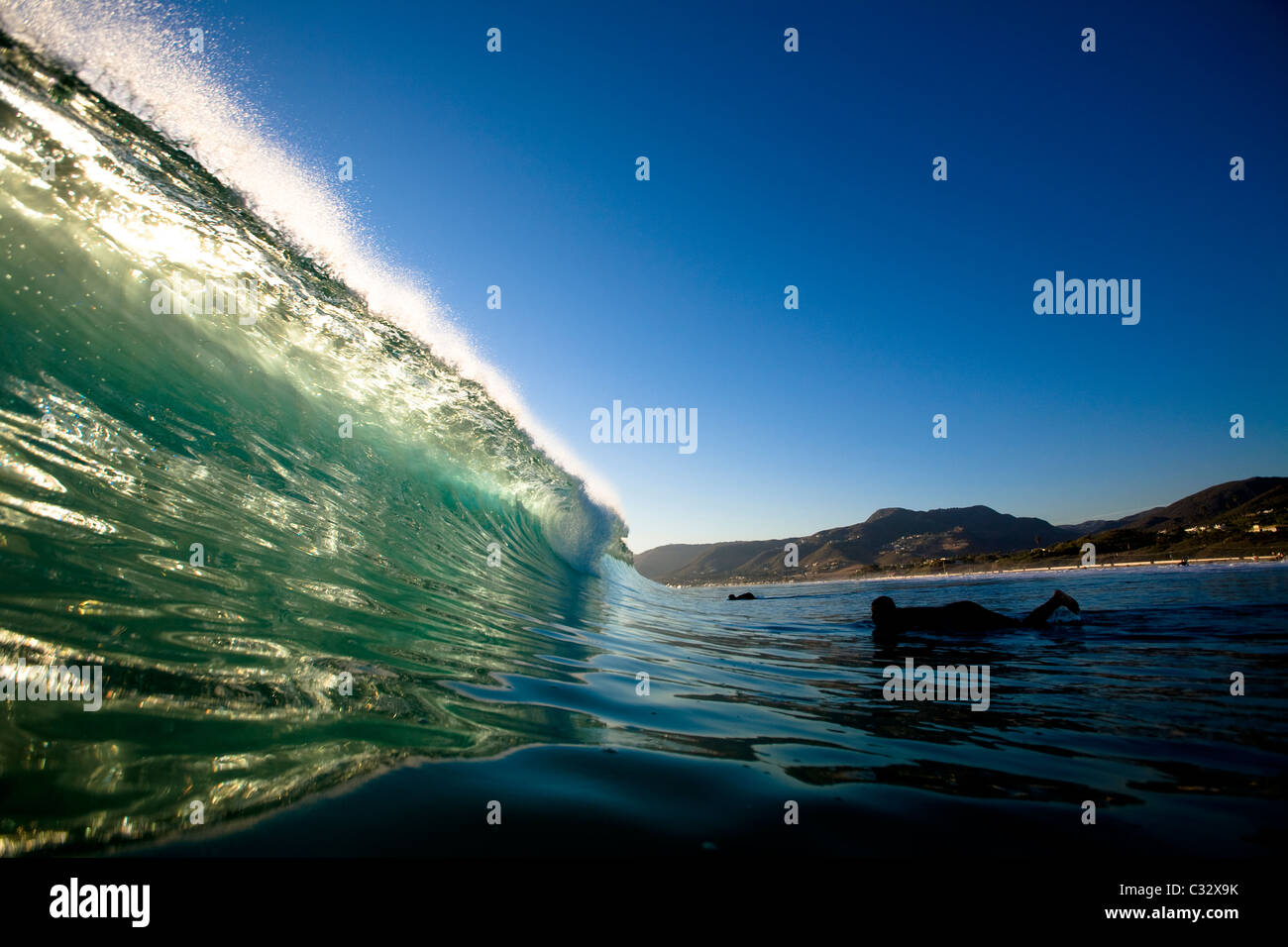 A male surfer gets ready to duck dive a backlit wave while surfing Zuma