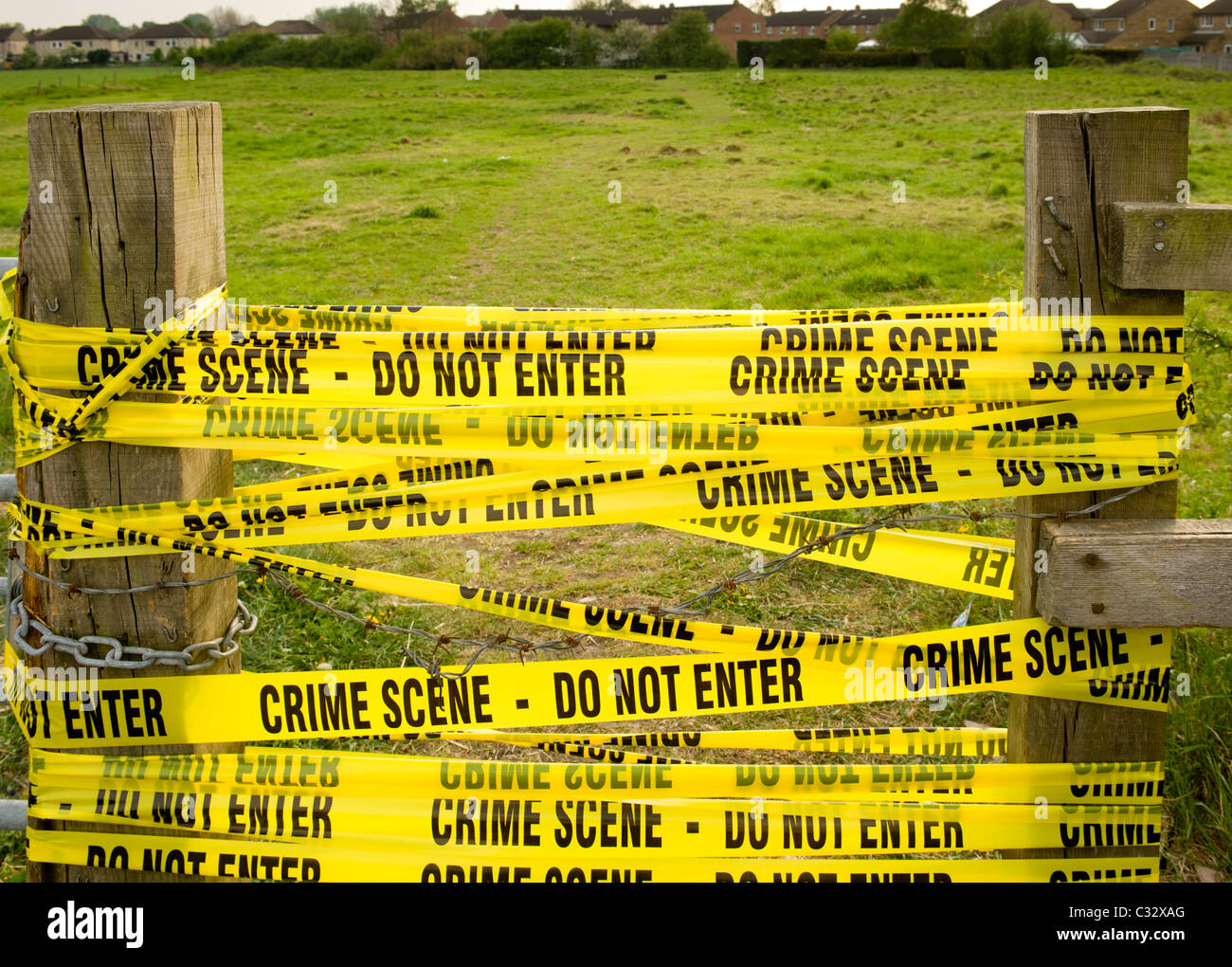 Yellow CRIME SCENE tape - Do not enter - between wooden posts with field in background. Stock Photo