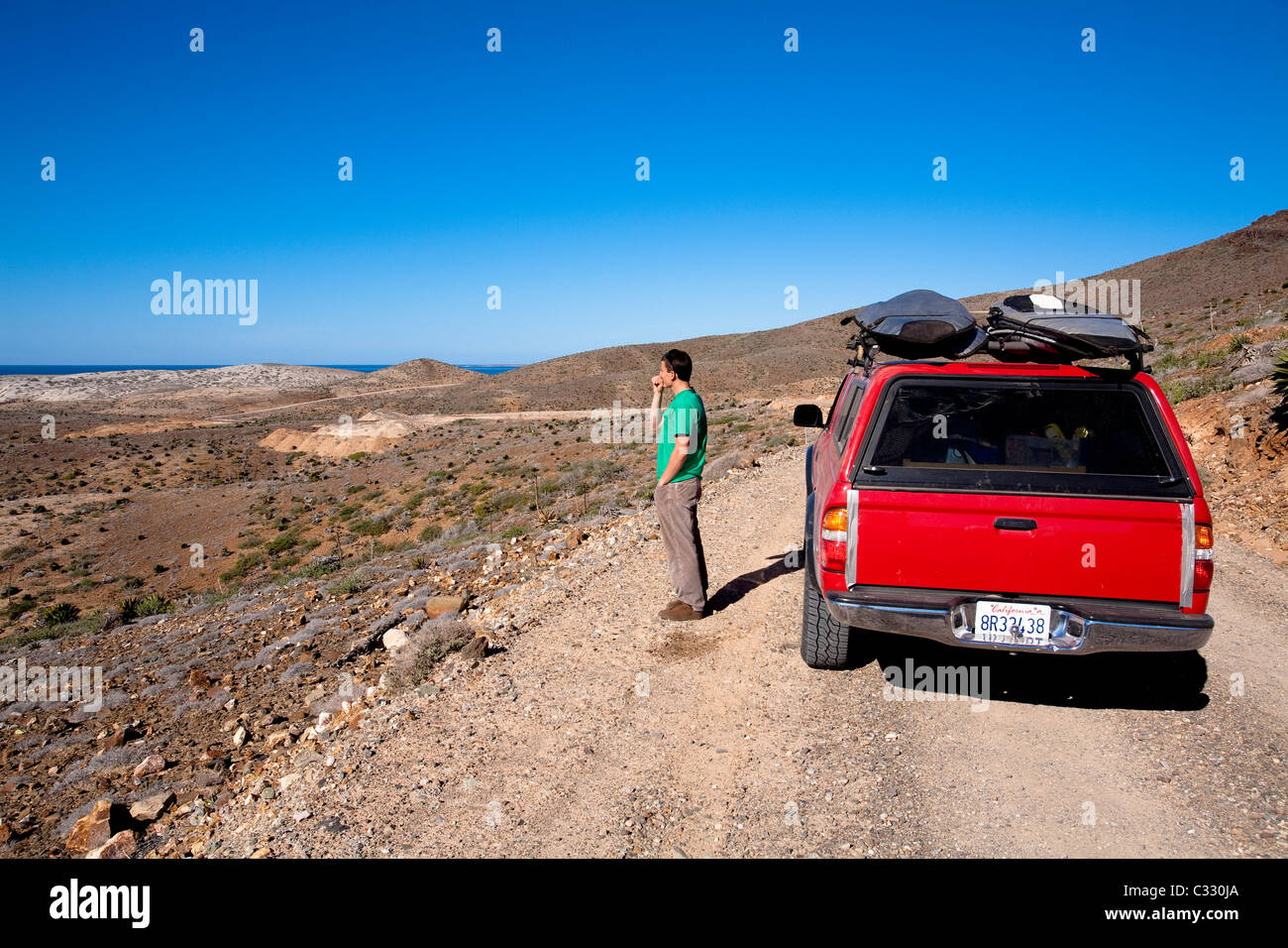 A male surfer looks out over the desert to check the surf in Baja, Mexico. Stock Photo