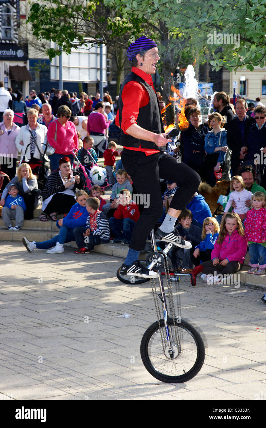 street entertainer on a unicycle with flaming torches in front of a crowd in the uk Stock Photo