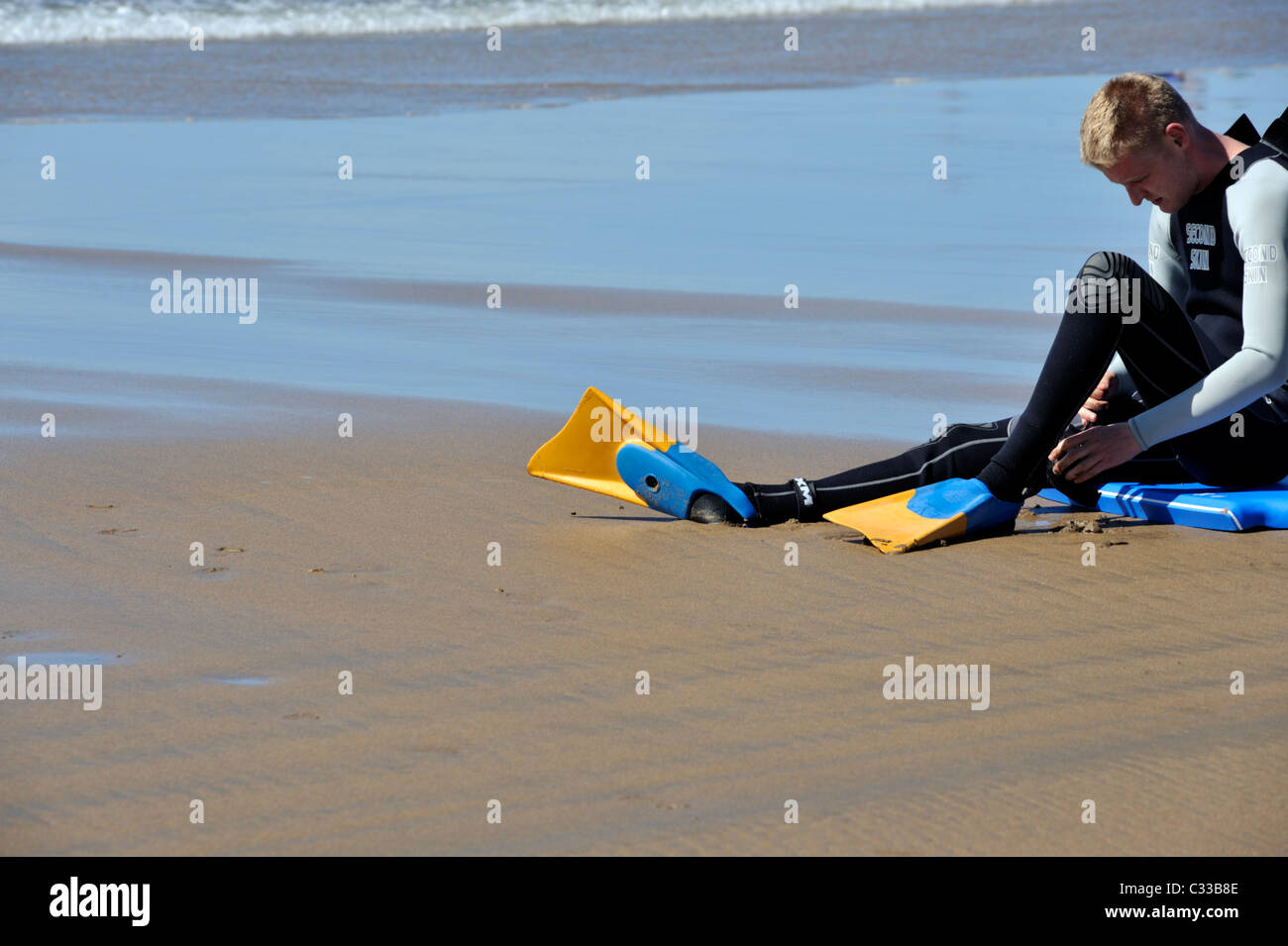 Surfer putting swimming fins on at Cornish beach Stock Photo