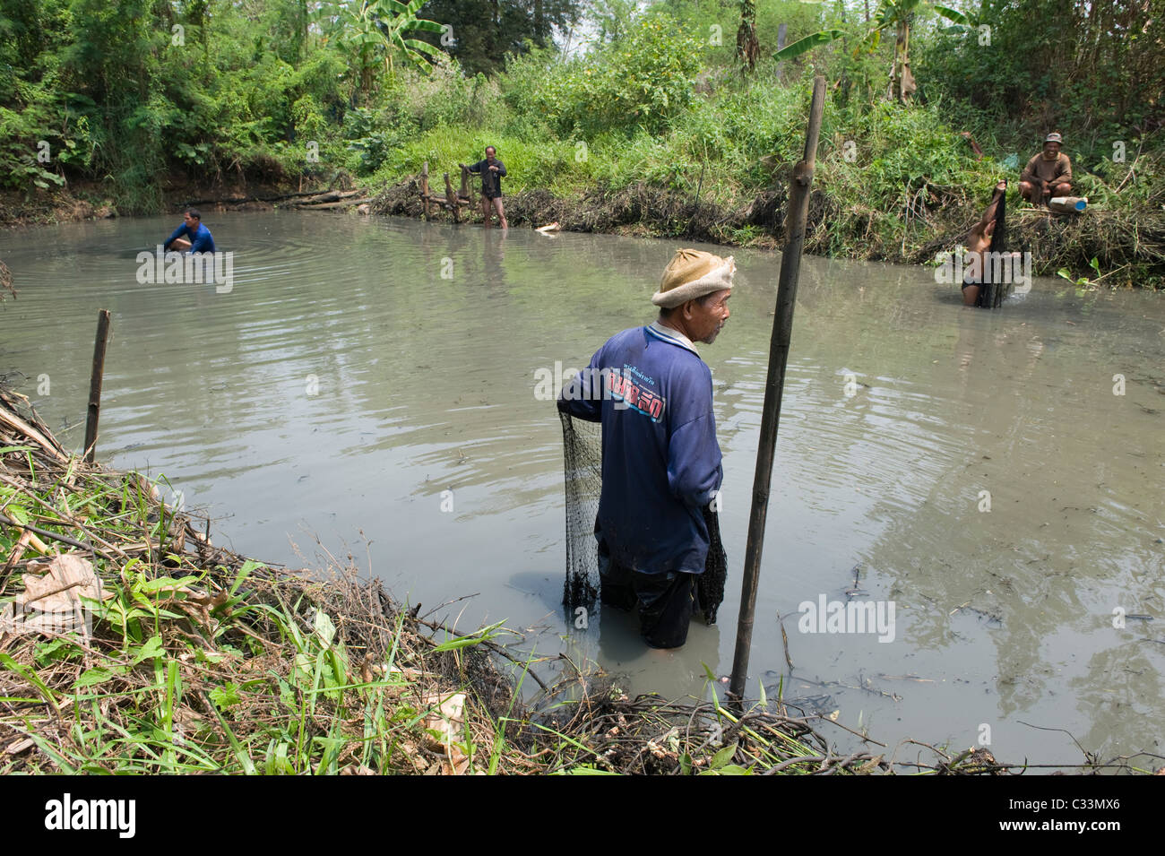 Thai men fishing in a drainage dyke canal in Isan North East Thailand. They use traditional weighted throwing nets. Stock Photo