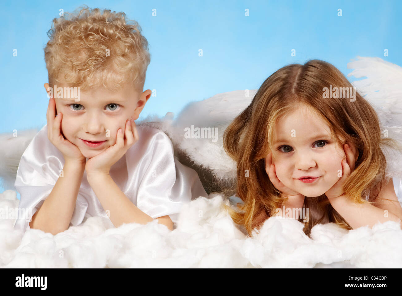 Small boy and girl in angelic costume lying on white cloud Stock Photo ...