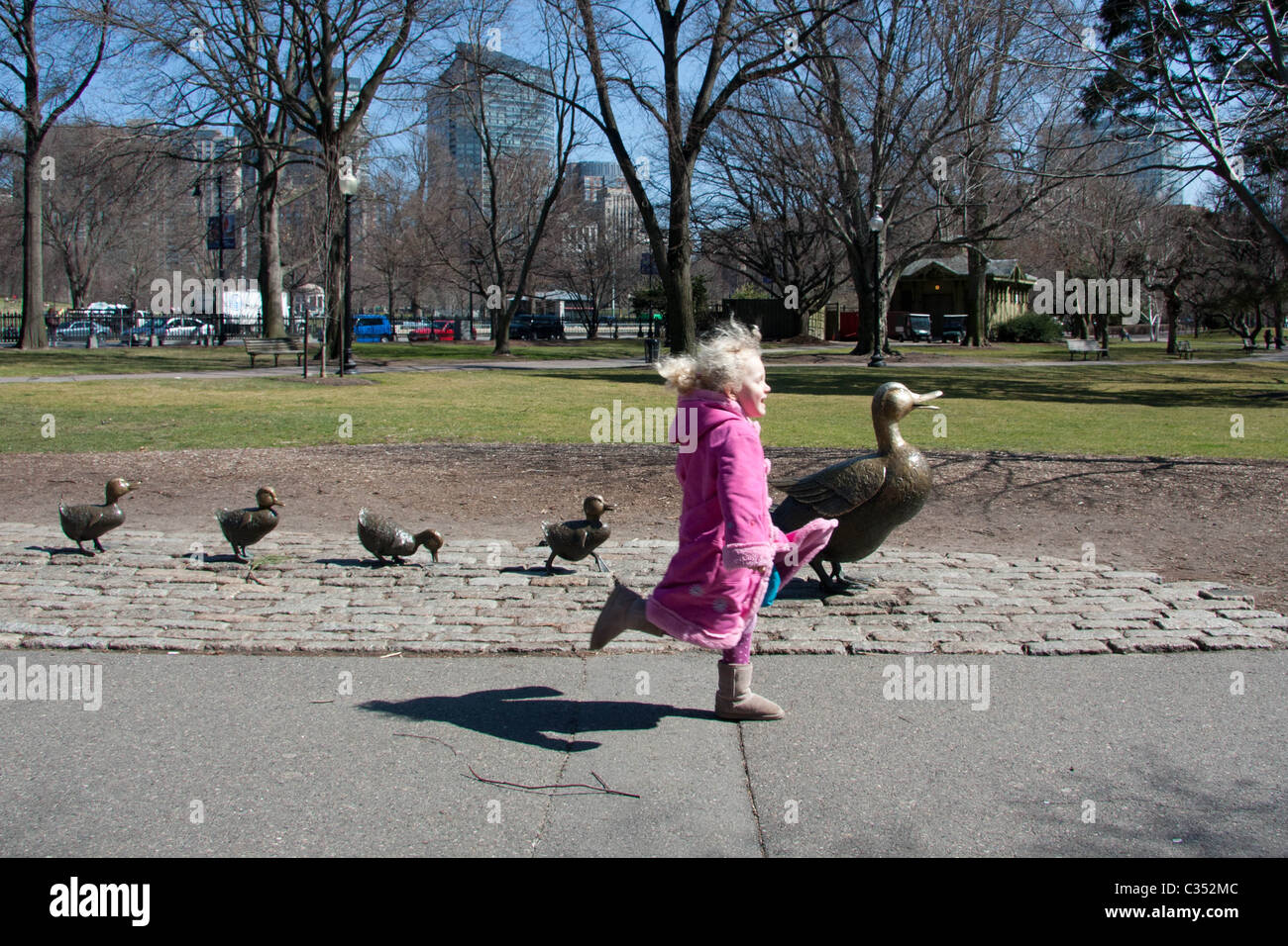 A girl in pink, running past the sculpture of a duck and her ducklings on Boston Common, Massachusetts Stock Photo