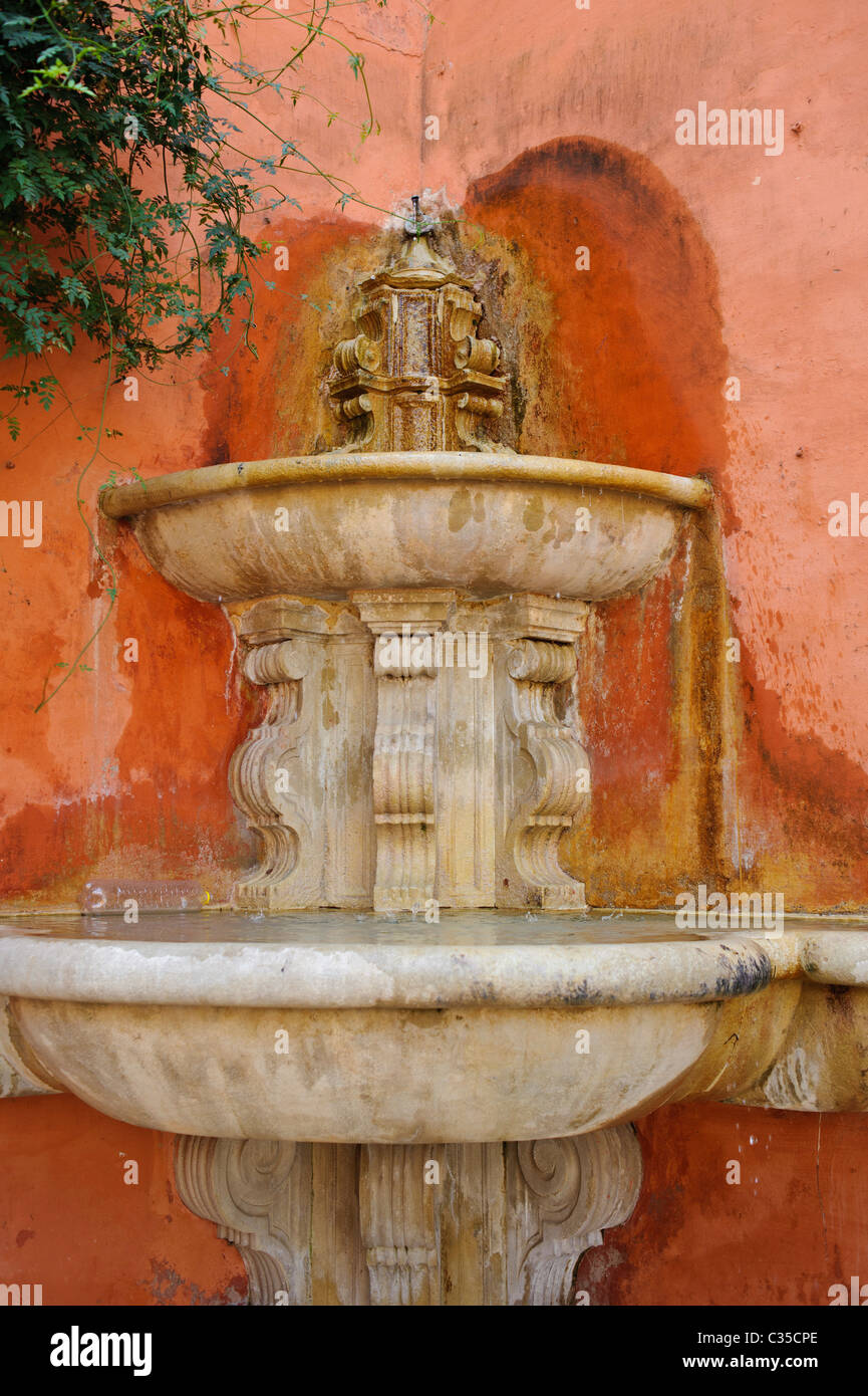 A marble fountain against an orange wall in Sevile Stock Photo