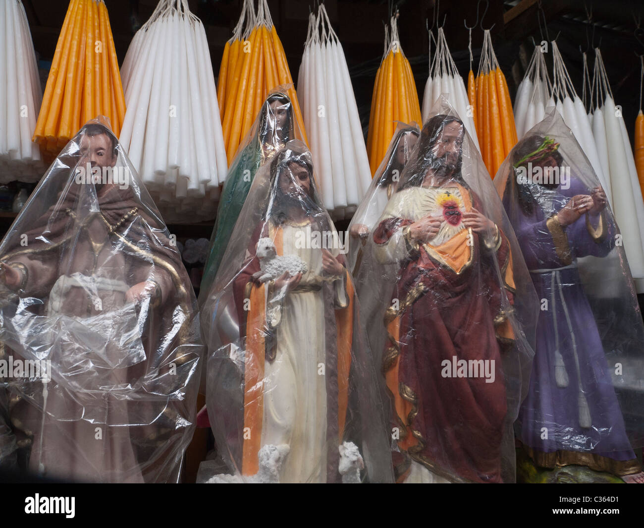 Small religious Catholic statues stand for sale covered in clear plastic in front of rows of
