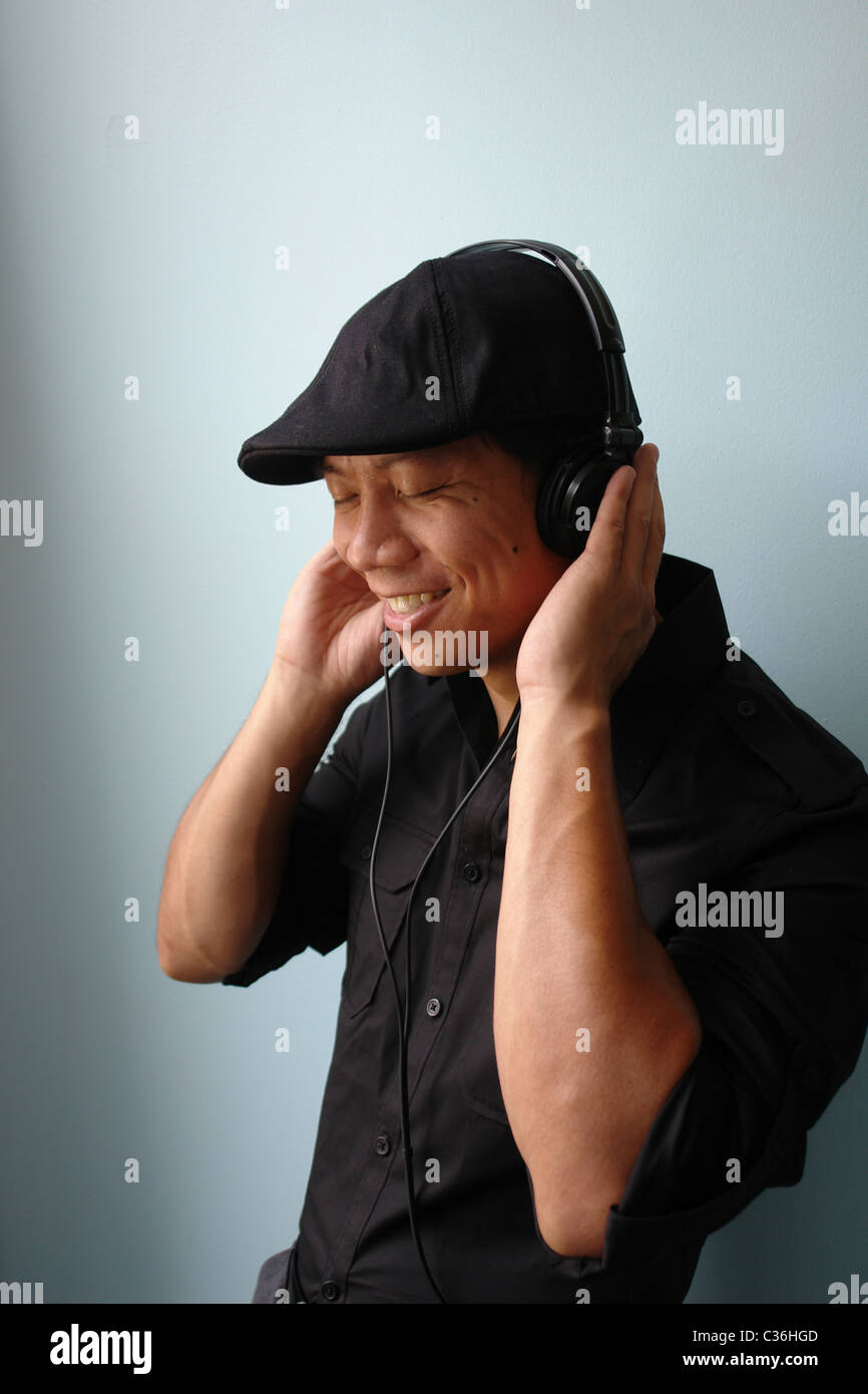Studio Portrait of Man Listening to Headphones with his Eyes Closed. He is Wearing a Black Shirt and Black Cap Hat  - Copy Space Stock Photo