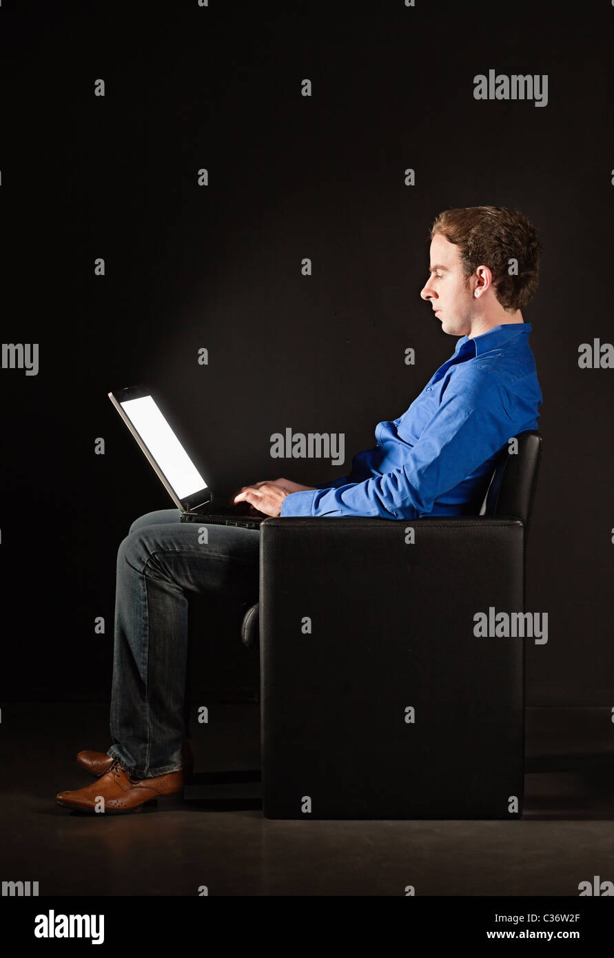 Young man sitting in the darkness with laptop, illuminated by the light from the screen Stock Photo