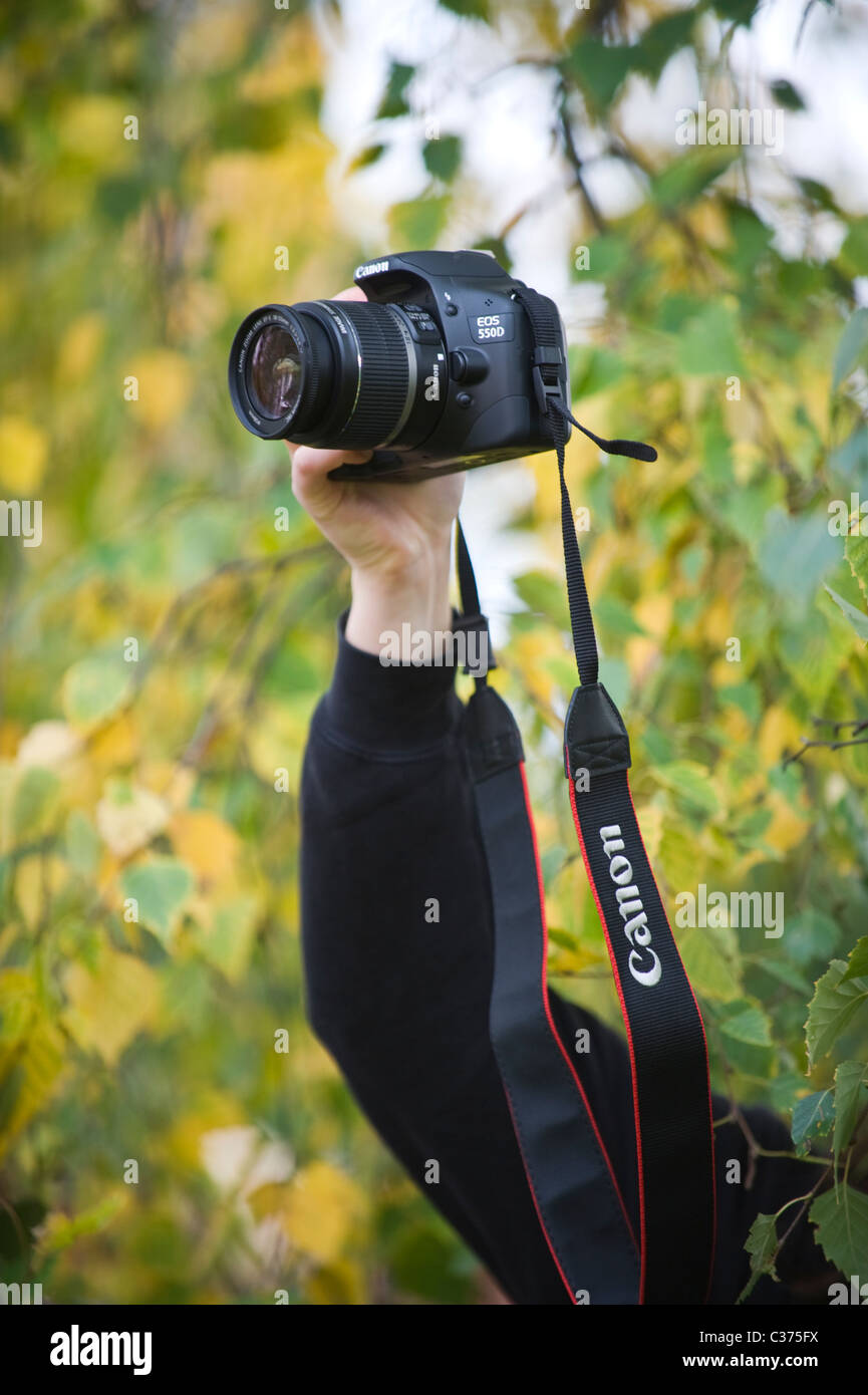 Young woman with Canon digital SLR camera taking photographs from cover of bushes Stock Photo
