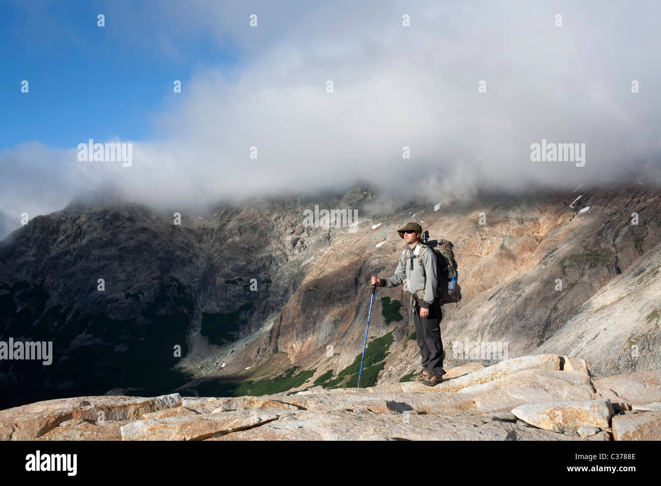 Hiker with backpack relaxing on top of a mountain and enjoying the ...