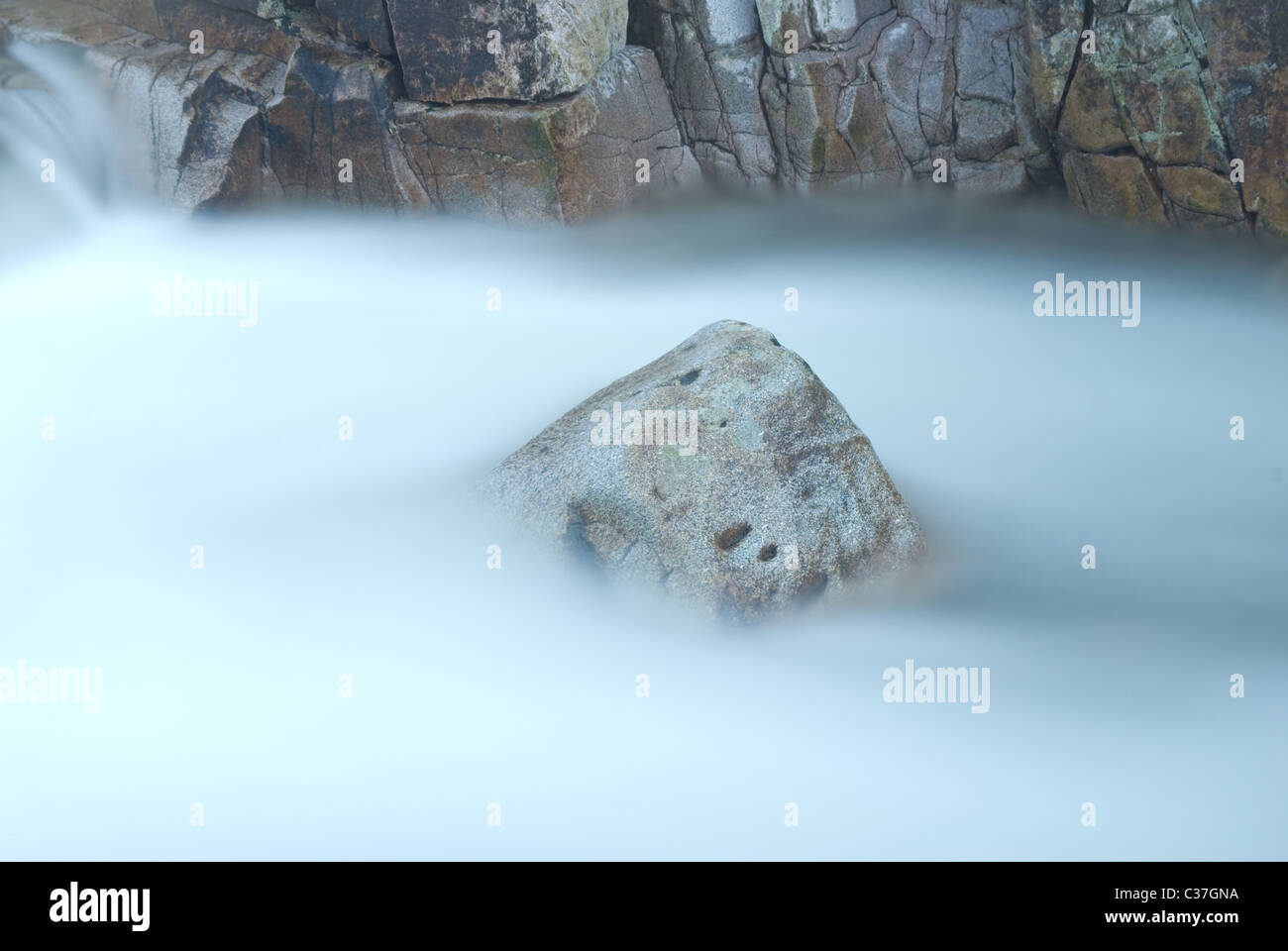 A rock stands in the river as the water flows past (time exposure) Stock Photo