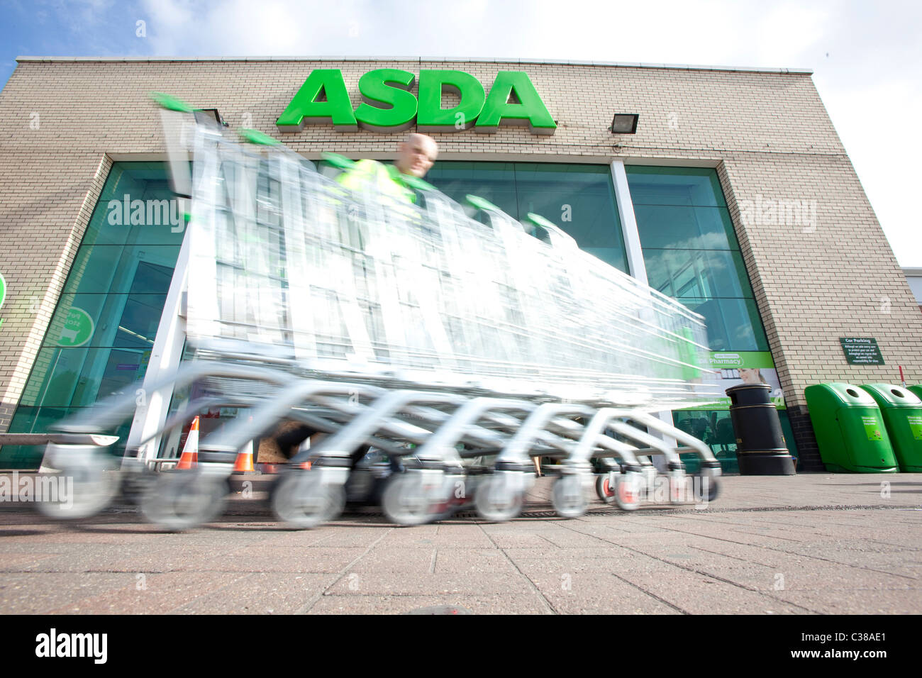 An employee collects trolleys outside an ASDA store. Stock Photo