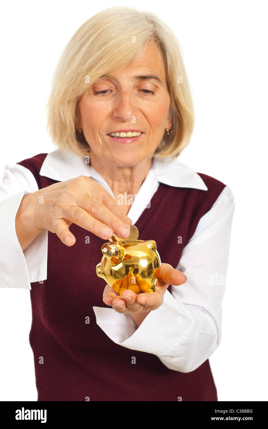 Senior smiling woman saving money and putting coin in a gold piggy bank ...
