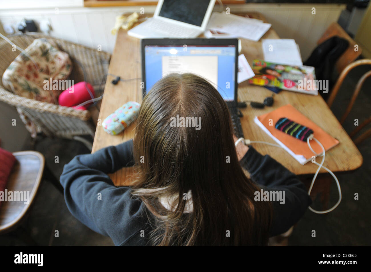 A 13 year old girl does her homework on a computer at a messy  kitchen table Stock Photo